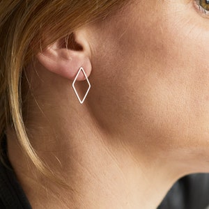 May include: A pair of silver diamond-shaped earrings. The earrings are simple and minimalist, with a thin wire frame.