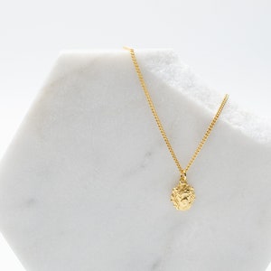 May include: A gold chain necklace with a small, textured, round pendant. The pendant appears to be a lion's head.
