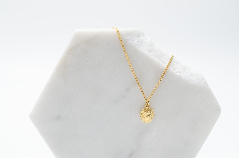 May include: A gold chain necklace with a small, textured, round pendant. The pendant appears to be a lion's head.