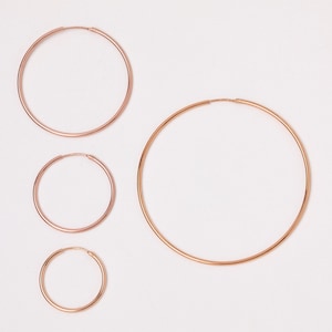 May include: Four gold hoop earrings of different sizes. The earrings are arranged in a row from largest to smallest.