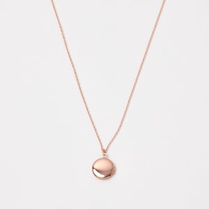 Könnte beinhalten: Halskette mit Medaillon aus Roségold. Die Halskette hat eine zarte Kette und einen runden Medaillon-Anhänger. Das Medaillon hat einen Durchmesser von etwa 2 cm. Die Halskette wird vor weißem Hintergrund präsentiert.