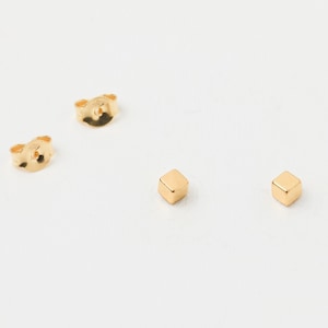 Könnte beinhalten: Ein Paar goldene quadratische Ohrstecker. Die Ohrringe sind klein und schlicht und würden ein tolles Accessoire für jeden Tag sein.