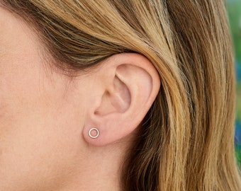 May include: A close-up of a person's ear with a small, thin, gold hoop earring. The earring is a simple circle shape.