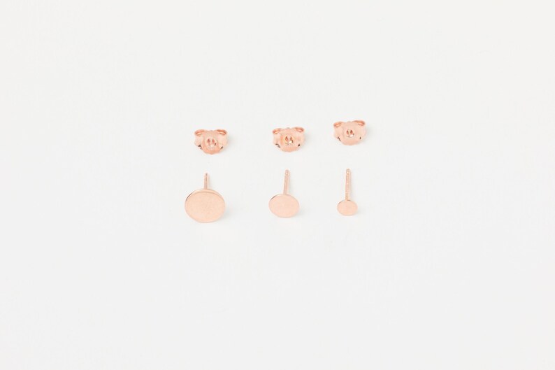 May include: Set of three rose gold stud earrings. The earrings feature a small, medium, and large round disc.
