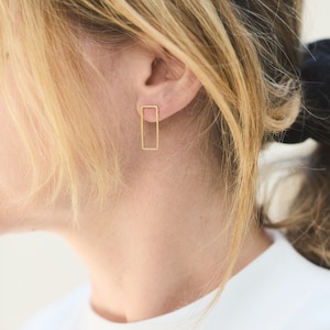 Könnte beinhalten: Eine Person trägt ein weißes Hemd mit einem goldenen rechteckigen Ohrring.