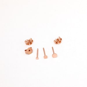 Könnte beinhalten: Ein Set aus Ohrringverschlüssen und Stiften in Roségold. Die Verschlüsse sind im Schmetterlings-Stil und die Stifte sind rund.