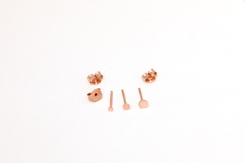 May include: A set of rose gold earring backs and posts. The backs are butterfly style and the posts are round.