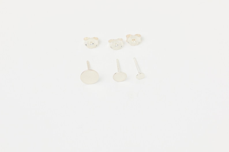 May include: Set of five silver stud earrings. Two earrings feature a small, round, silver design. Three earrings feature a larger, round, silver design.