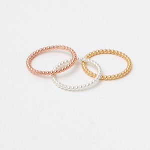 Könnte beinhalten: Drei Perlenringe in Gold, Silber und Roségold. Die Ringe sind übereinander gestapelt.