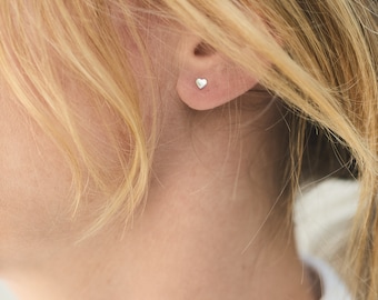 May include: A close-up of a person's ear with a small silver heart-shaped stud earring.