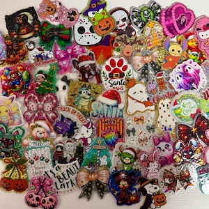 May include: A collection of assorted decorative acrylic charms featuring various pop culture characters, holiday themes, glittery bows, and seasonal motifs including pumpkins, ghosts, and Christmas elements, all with a glossy finish.