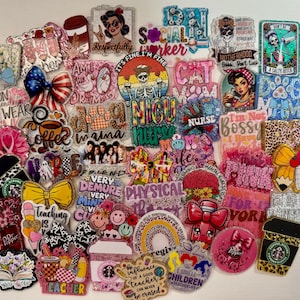 May include: A collection of colorful acrylic badge reels with various designs and text. The reels feature bows, coffee cups, and phrases like "Social Worker," "Nurse," and "Teacher." The color palette includes pink, yellow, and blue.