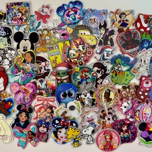 May include: A collection of colorful character-themed acrylic pins featuring Disney, Marvel, and other pop culture icons. The pins showcase various designs, including cartoon characters, movie scenes, and logos, with glitter and vibrant colors.