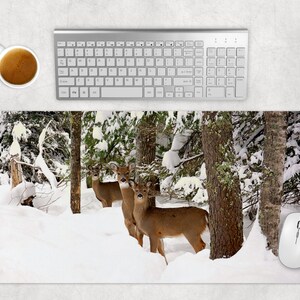 Può includere: Una scena di bosco invernale con tre cervi dalla coda bianca in piedi nella neve. I cervi sono marroni e bianchi con grandi corna. Il bosco è ricoperto di neve e gli alberi sono spogli. Un mouse per computer si trova nell'angolo in basso a destra dell'immagine.