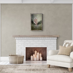 May include: A white owl with brown markings sits on a branch in a snowy forest. The image is framed in a rustic wooden frame and hangs above a white brick fireplace.