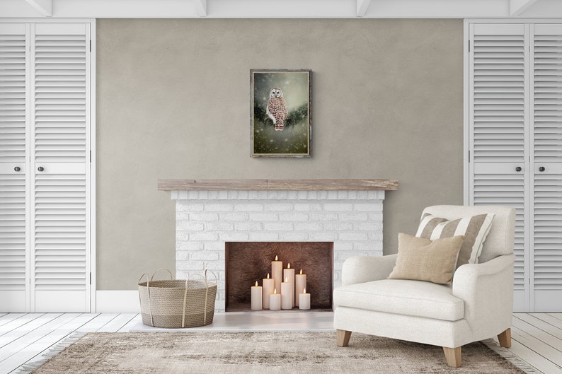 May include: A white owl with brown markings sits on a branch in a snowy forest. The image is framed in a rustic wooden frame and hangs above a white brick fireplace.