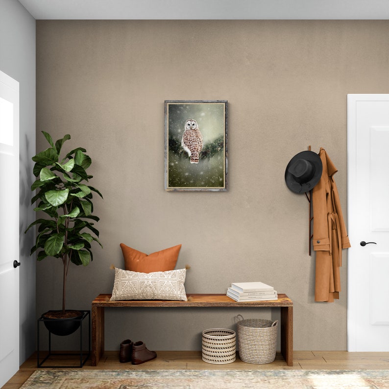 May include: A framed print of a snowy owl perched on a branch in a wintery forest setting. The print is hanging on a light brown wall above a wooden bench with a pillow, books, and baskets.
