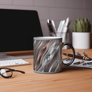 May include: A black and white colour changing mug with a swirling abstract design. The mug is on a wooden table with a keyboard and glasses.