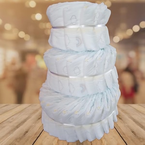 May include: A stack of white baby diapers, secured with silver ribbon. Each diaper features a cloud and rainbow design. The diapers are stacked on a wooden surface with a blurred background.