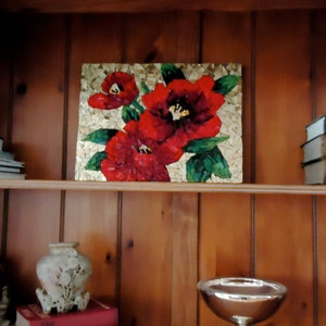 K&ouml;nnte beinhalten: Ein rechteckiges Mosaikkunstwerk mit leuchtend roten Blumen mit schwarzen Zentren und gr&uuml;nen Bl&auml;ttern. Das Kunstwerk ist vor einem goldfarbenen Hintergrund platziert und auf einem Holzregal ausgestellt. Das Regal ist Teil eines Holzschranks.