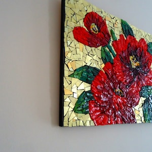 K&ouml;nnte beinhalten: Ein Mosaikkunstwerk mit roten Blumen und gr&uuml;nen Bl&auml;ttern vor goldenem Hintergrund. Das Mosaik besteht aus kleinen, unregelm&auml;&szlig;ig geformten Fliesen, die einen strukturierten Effekt erzeugen. Das Kunstwerk ist auf einem schwarzen Rahmen montiert.