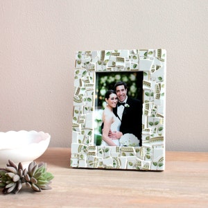 May include: A rectangular photo frame with a mosaic design. The frame is white with green and gold accents. The photo inside shows a smiling couple in formal wedding attire. The frame is on a wooden surface.