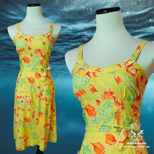 May include: A yellow sundress with a fish and seaweed pattern in orange and green. The dress has a fitted bodice, a tie waist, and a knee-length skirt. The dress is displayed on a mannequin.