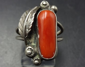 May include: A silver ring with a red coral stone and a leaf design. The ring is set on a white background.