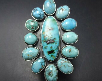 May include: A silver ring featuring a large oval turquoise stone surrounded by 12 smaller turquoise stones.
