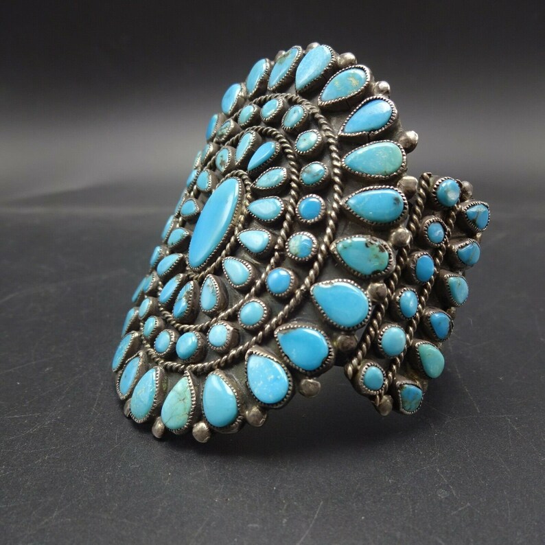 May include: A silver cuff bracelet with a large turquoise stone design. The bracelet is made of sterling silver and features a cluster of turquoise stones in a circular pattern.
