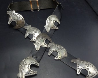 Könnte beinhalten: Ein schwarzer Ledergürtel mit sieben silbernen Bärenpfoten-Conchos. Die Conchos sind mit geometrischen Mustern verziert.