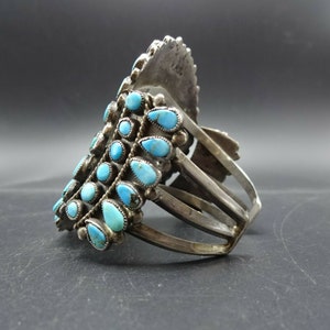 May include: A silver bracelet with a cluster of turquoise stones in a graduated pattern. The bracelet has a stamped mark "K.M.S."