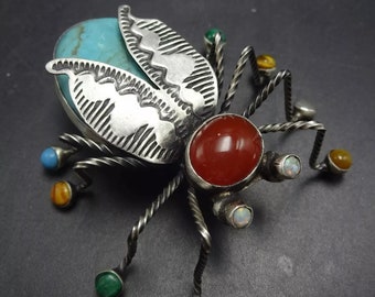 May include: A silver and turquoise beetle brooch with a red carnelian stone and other colorful stones. The beetle has detailed wings and a twisted wire body.