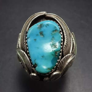 May include: A turquoise ring with a silver setting. The turquoise is a bright blue colour and is set in a silver band with a design of feathers. The ring is a statement piece and would be a great addition to any jewellery collection.