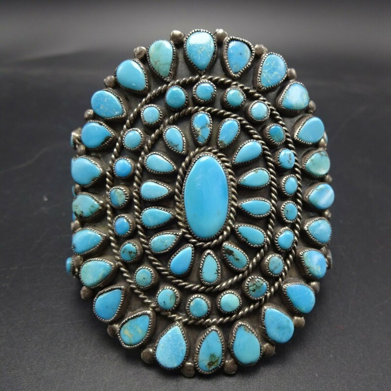 May include: A silver and turquoise Native American bracelet with a large oval turquoise stone in the center surrounded by smaller turquoise stones.