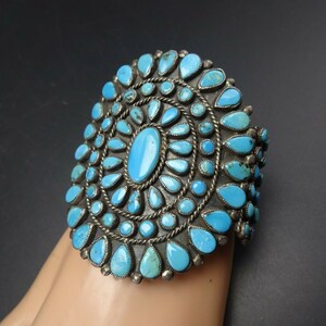 May include: A silver cuff bracelet with a large turquoise stone cluster in a sunburst design.