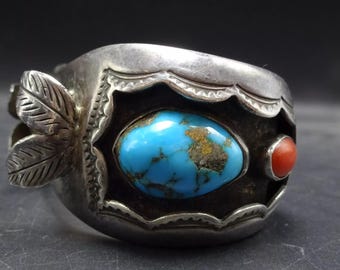 Puede incluir: Un brazalete de plata con incrustaciones de turquesa y coral. El brazalete tiene un diseño de hoja en un lado y un borde festoneado en el otro.