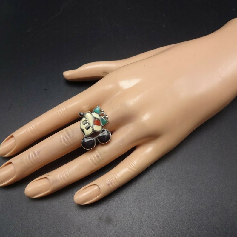 May include: A silver ring with a colorful inlay depicting a cartoon character's face. The character has black ears, a white face, and a red and green hat.