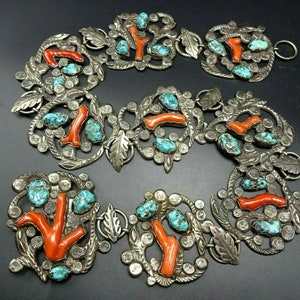 May include: A silver-toned belt featuring coral and turquoise stones. The belt is composed of several ornate, circular links with leaf and floral designs. The coral is a vibrant orange-red, and the turquoise is a bright blue-green.
