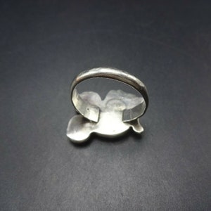 May include: A silver ring with a detailed design of a bird in flight. The ring is shown from the back, revealing the smooth band.