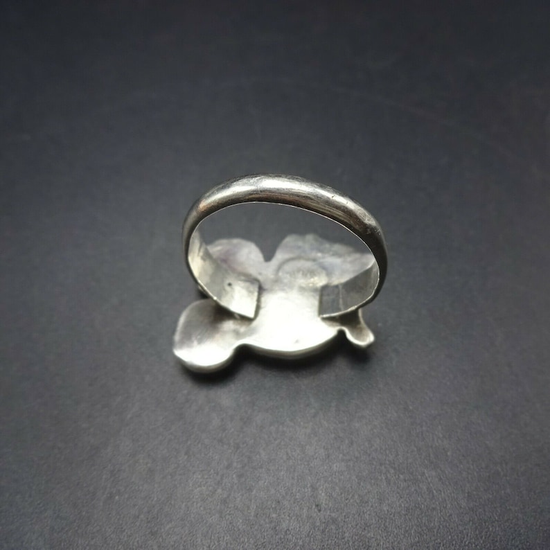 May include: A silver ring with a detailed design of a bird in flight. The ring is shown from the back, revealing the smooth band.