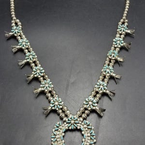 Puede incluir: Un collar de plata y turquesa con un colgante de media luna. El collar está hecho de pequeñas cuentas de plata y tiene un diseño floral con piedras turquesa.