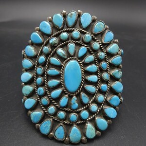 May include: A silver and turquoise Native American bracelet with a large oval turquoise stone in the center surrounded by smaller turquoise stones.