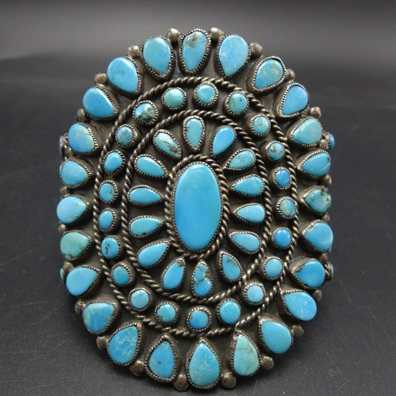 May include: A silver and turquoise Native American bracelet with a large oval turquoise stone in the center surrounded by smaller turquoise stones.