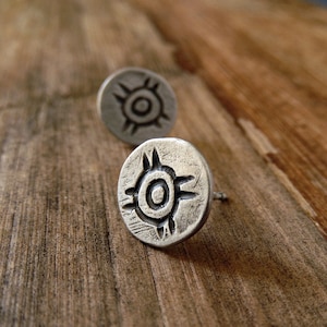 Könnte beinhalten: Ein Paar silberne Ohrringe mit einem runden Design, das eine stilisierte Sonne mit Strahlen und einen Kreis in der Mitte zeigt.