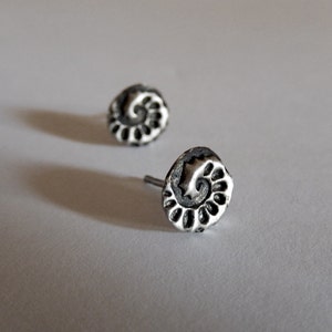 Puede incluir: Un par de pendientes de plata con un diseño en espiral. Los pendientes son pequeños y delicados, y serían un gran regalo para un amigo o un ser querido.