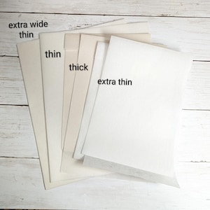 May include: A selection of paper samples, with labels indicating different thicknesses: "extra wide thin", "thin", "thick", and "extra thin". The papers are in shades of cream and white, displayed on a light wood-effect surface.