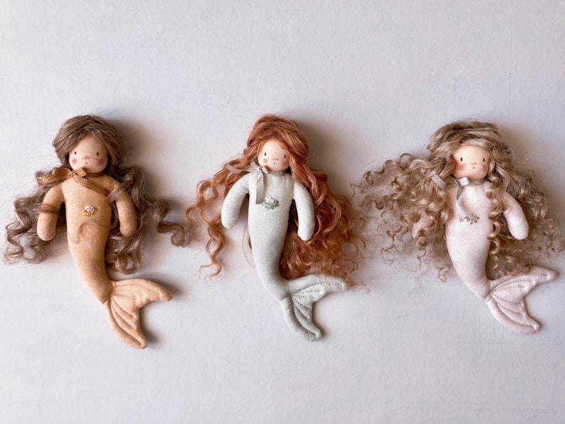 May include: Three handmade mermaid dolls with curly hair. The dolls are wearing different colored outfits. The dolls are made of fabric and have embroidered details.