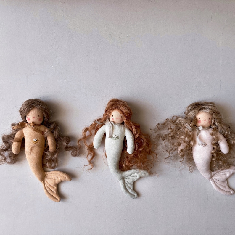 May include: Three handmade fabric mermaid dolls with curly hair. The dolls are wearing different colored outfits: brown, light green, and pink.