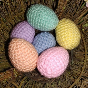 May include: Six crocheted Easter eggs in a nest of twigs. The eggs are in pastel colors: light blue, pink, peach, yellow, lavender, and green.
